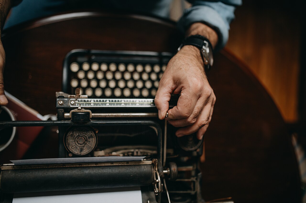 A person's hands adjusting the mechanism of an old black typewriter, close-up.